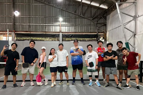 Group of eleven young adults posing and smiling on an indoor pickleball court under bright lights just finished a session that was run using fairplay pickleball app