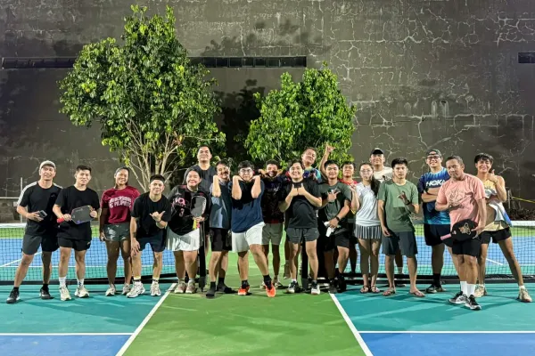 Group of people standing on a pickleball court holding paddles, smiling and posing for a photo at night. just finished a session that was run using fairplay pickleball app