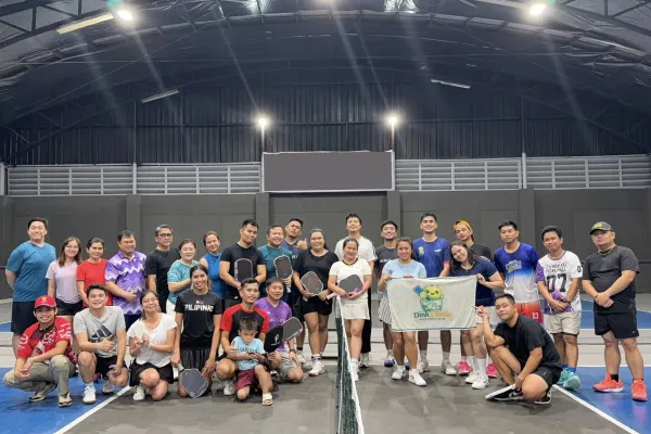 Group of 30 people posing on an indoor pickleball court, some holding paddles and a banner with a turtle graphic. just finished a session that was run using fairplay pickleball app