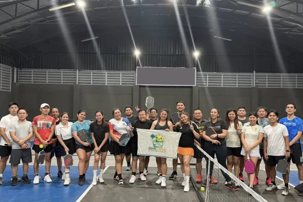 Group of men and women posing with pickleball paddles on an indoor court under bright lights. just finished a session that was run using fairplay pickleball app