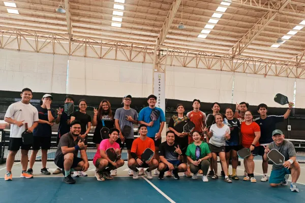 Group of 18 diverse people posing with pickleball paddles on an indoor court under a high roof. just finished a session that was run using fairplay pickleball app