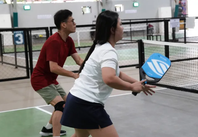 Two people playing pickleball indoors with rackets, focused on the game near the net.
