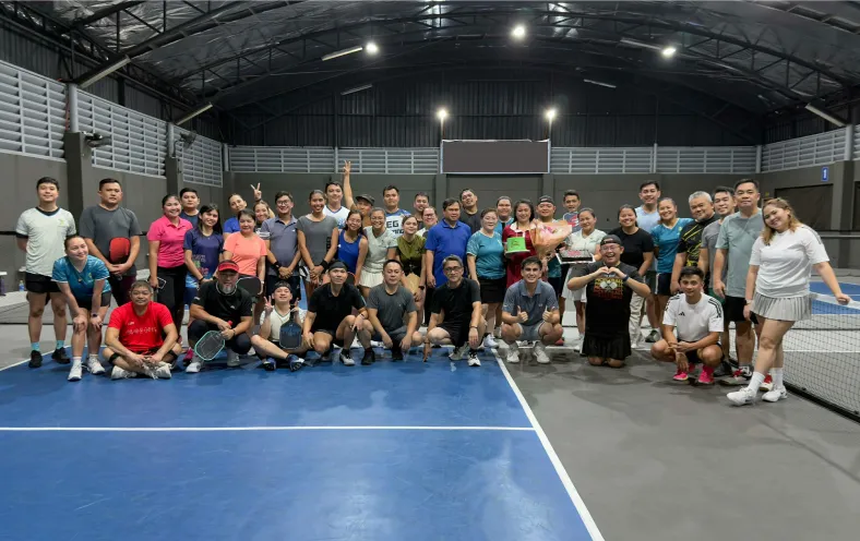 Group of adults posing on an indoor pickleball court, some holding paddles and trophies. just finished a session that was run using fairplay pickleball app