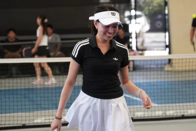 Smiling female pickleball player wearing a black shirt and white skirt standing on an indoor pickleball court.